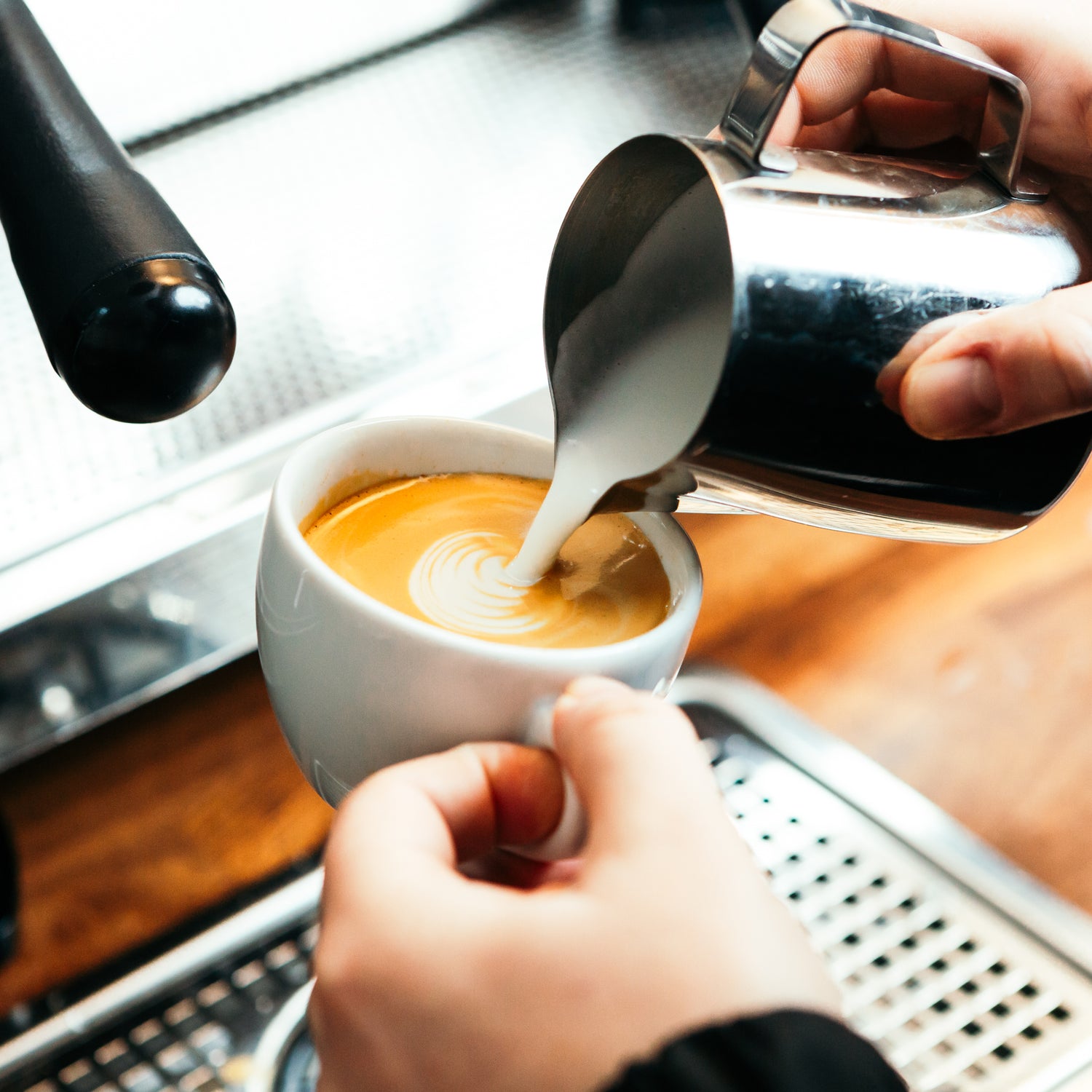 Steamed milk pouring into flat white cup with espresso. The beginnings of latte art forming.