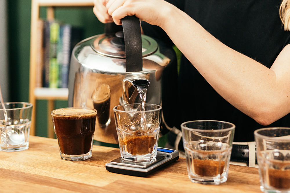Kettle pouring water into coffee cupping glasses