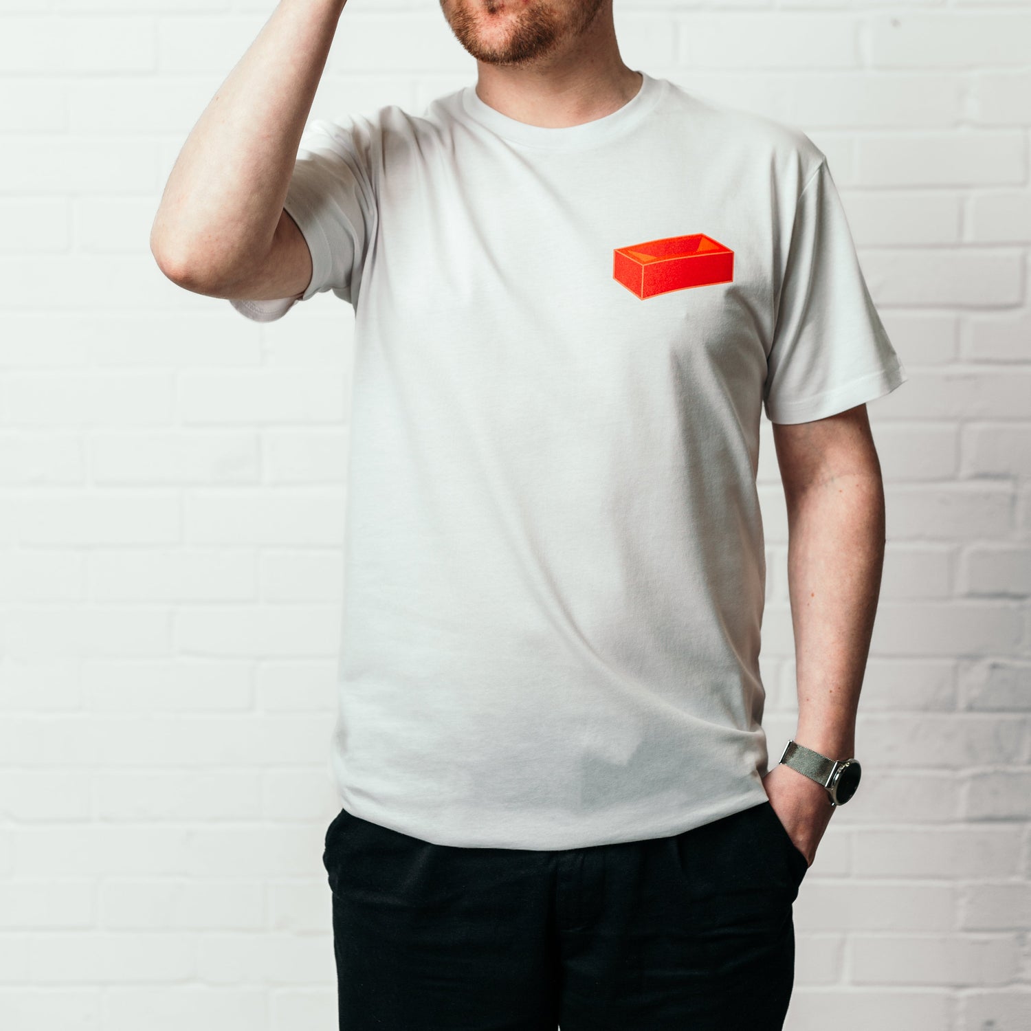 A man wearing a white t-shirt with a red brick printed on the top left.