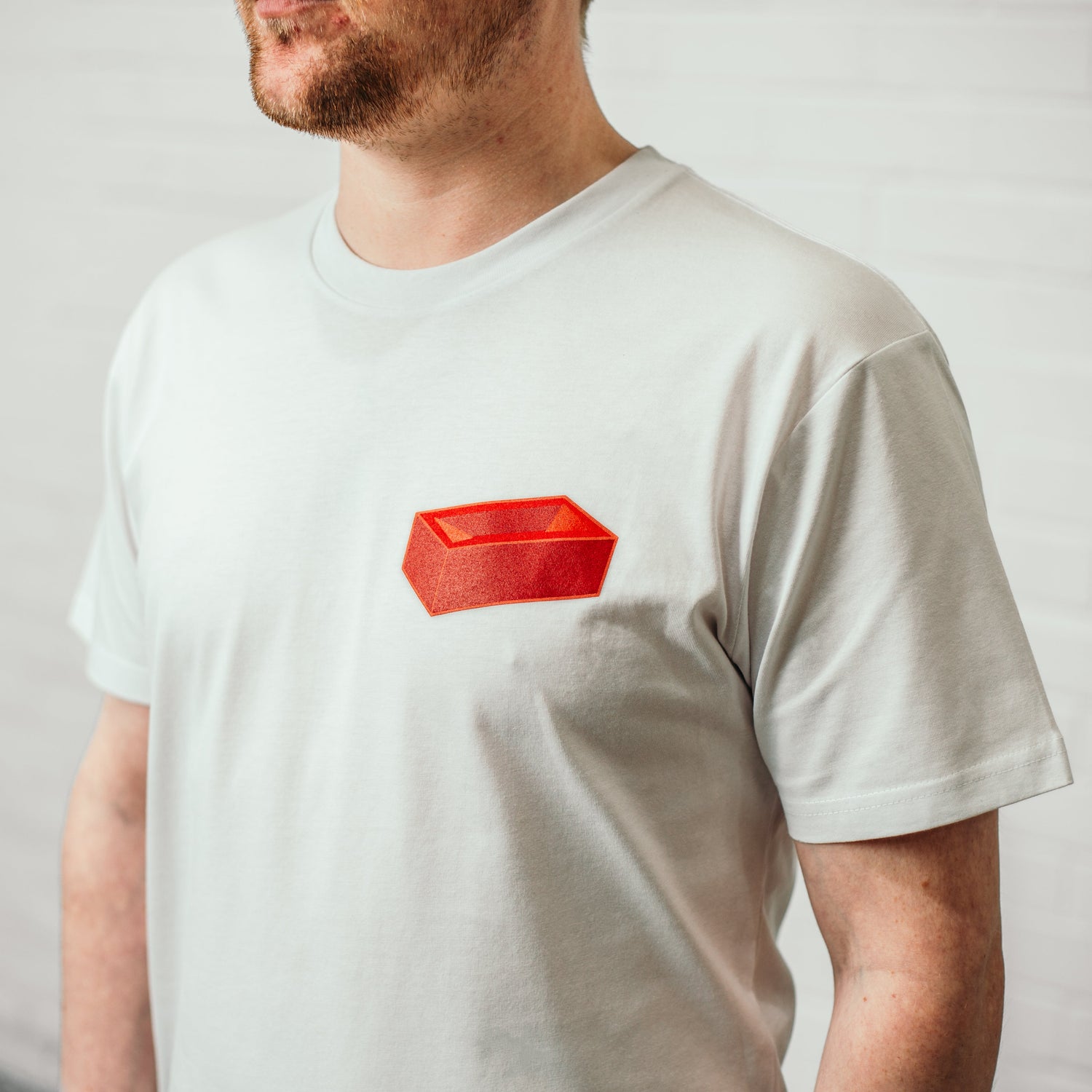 A man wearing a white t-shirt with a red brick printed on the top left.